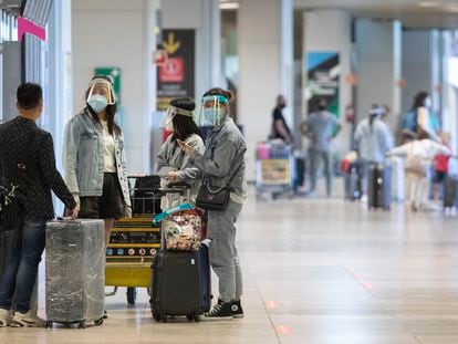 Varias personas protegidas con mascarillas y pantallas protectoras en el aeropuerto Madrid-Barajas.