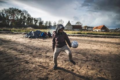 Un joven juega al fútbol en un campamento improvisado en la periferia de Calais (Francia), donde migrantes de diversas nacionalidades aguardan para intentar alcanzar el Reino Unido.