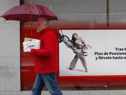 Una persona pasa delante de la una sucursal de Banco Santander donde se promocionan planes de pensiones.