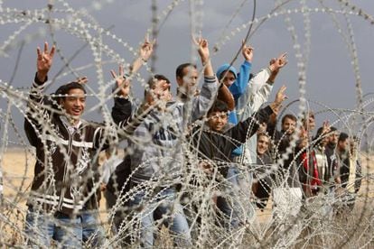 Un grupo de palestinos hacen gestos de victoria junto a una alambrada de la frontera entre el sur de Gaza e Israel.