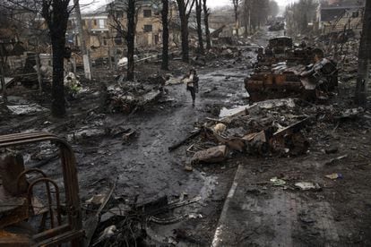 A woman walks between destroyed armored vehicles in Bucha.