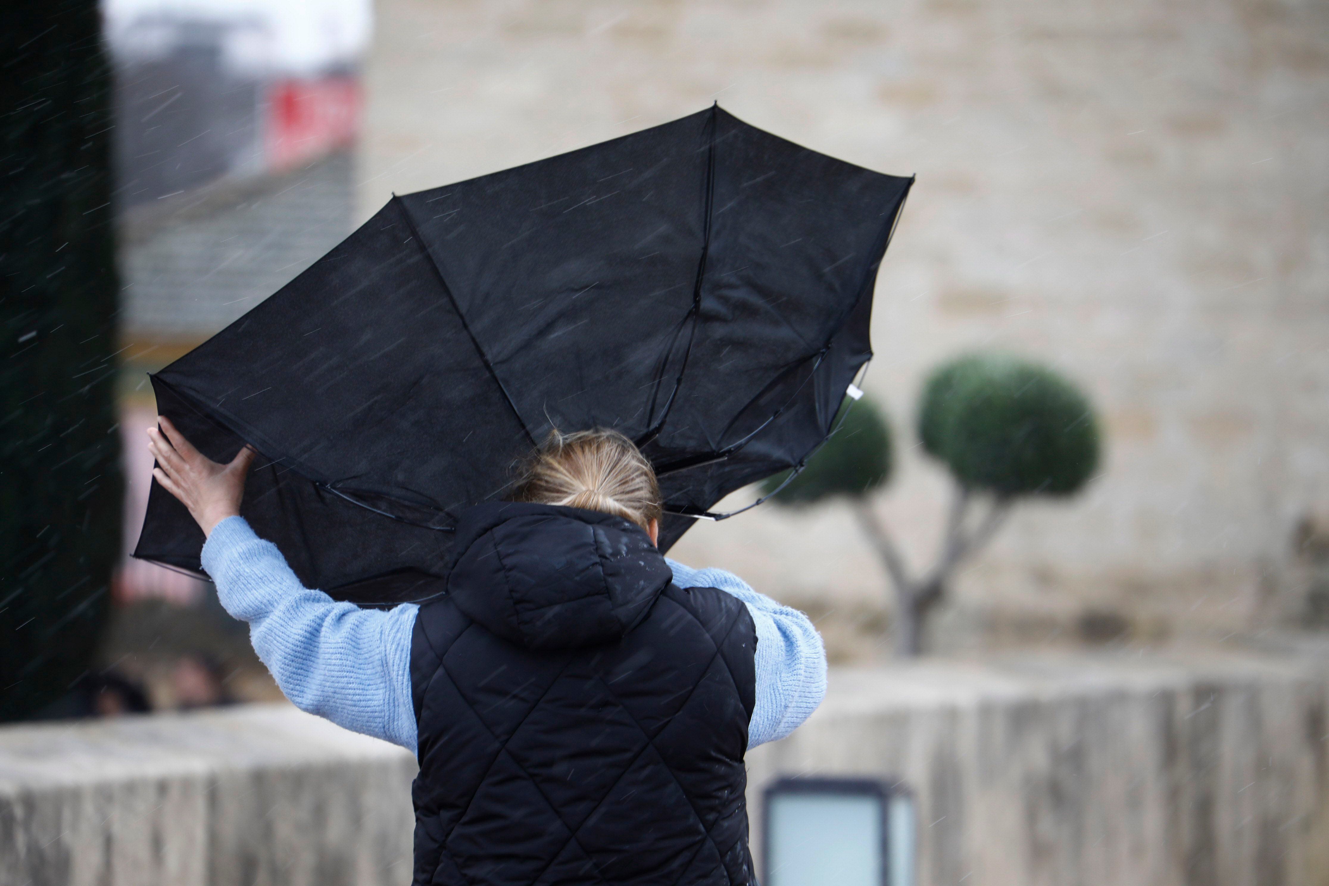 Una mujer intenta sujetar su paraguas mientras camina por el casco histórico de Córdoba, este viernes.