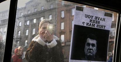 Una mujer ucrania toma una fotograf&iacute;a de un letrero de &quot;Se busca&quot; del presidente V&iacute;ctor Yanuk&oacute;vich.