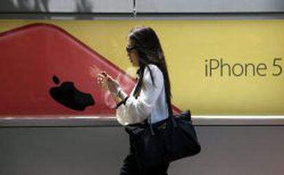 Una mujer utiliza un smartphone mientras camina junto a una publicidad de iPhone 5.