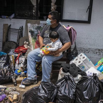 Un hombre cuida de un bebé al exterior de su casa que quedó dañada por las fuertes lluvias de la tarde el lunes en Atizapán, Estado de México