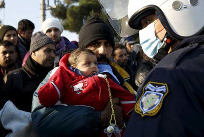 Un refugiado con su hijo en brazos, frente a un cordón de policía griega mientras espera para cruzar la frontera entre Grecia y Macedonia.