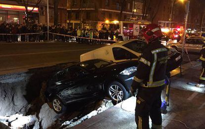 Los bomberos, delante de los coches que han caído dentro del socavón.