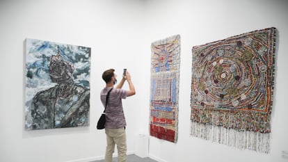 Un visitante fotografía las obras de los ugandeses Emmie Nume ('Dreaming of the sky', a la izquierda) y Sanaa Gatej ('She waits' y 'Galactic'), expuestas en ARCOLisboa, en la Cordoaria Nacional.