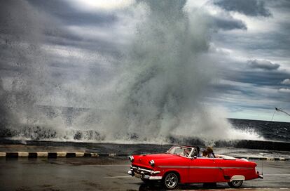 Un descapotable estadounidense de los años cincuenta en el paseo del Malecón de La Habana, con el agua saltando sobre el rompeolas.