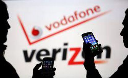 Dos usuarios manejan sus m&oacute;viles ante los logotipos de Vodafone y Verizon.