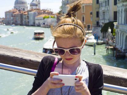 Una joven turista consulta su móvil en Venecia, con la cúpula de la iglesia de Santa María de la Salud al fondo.