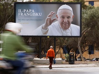Un hombre camina delante de una valla publicitaria que anuncia la llegada de Francisco a Malta.