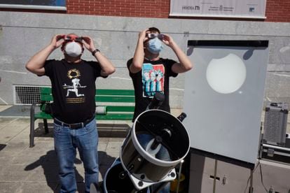 Dos personas miran con gafas espaciales el eclipse parcial del 10 de junio de 2021 en la explanada del Planetario de Pamplona, que también se proyecta de manera segura para observarlo usando un telescopio.