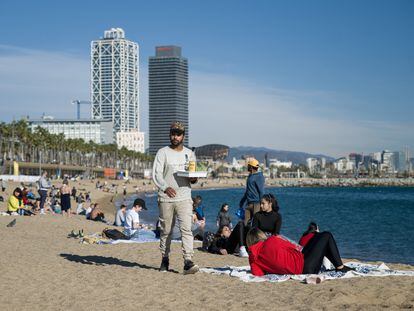 Un camarero lleva bebidas a las personas que disfrutan de las altas temperaturas en la playa de la Barceloneta, el pasado 25 de diciembre.