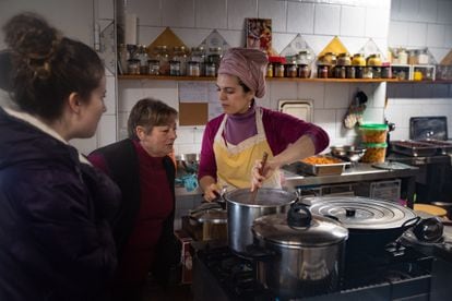 Maite López enseña la comida que está cocinando para la comunidad hinduista a Rosa Campesino y Esther Martín, naturales de Brandilanes.