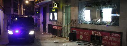 Un furgón de la policía pasa por delante de una sucursal de Bankia con los cristales rotos.