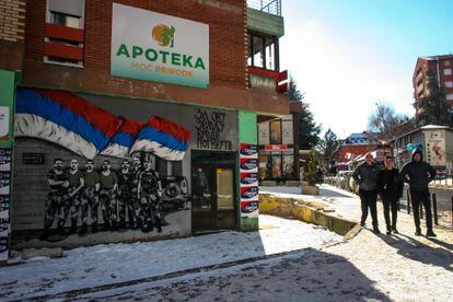 Tres jóvenes pasan junto a un mural en homenaje a los soldados de la batalla de Kosare de 1999 con la frase “Merece la pena dar la vida por este país”, en el norte de Mitrovica.