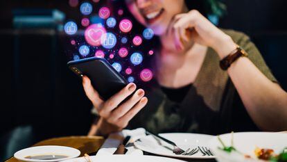 Joven sonriente usando un smartphone en una aplicación de redes sociales mientras disfruta de una comida en el restaurante, mirando o dando 'me gusta', amor, comentarios, agregando amigos y visitando páginas. Concepto de adicción a las redes sociales.