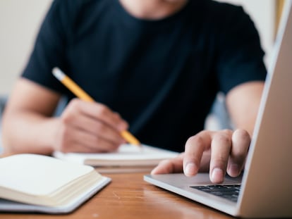 Un joven escribe a mano mientras consulta el ordenador.