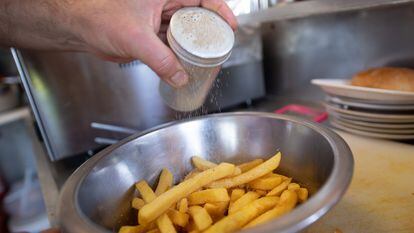Un hombre echa sal en un recipiente con patatas fritas.