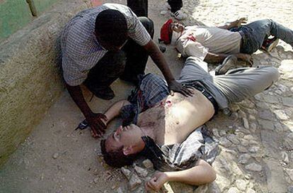 Un haitiano socorre a Ricardo Ortega, caído en el suelo después de recibir dos disparos ayer en Puerto Príncipe.