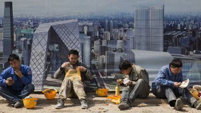 Varios obreros comen ante una imagen del distrito financiero de Pek&iacute;n.
