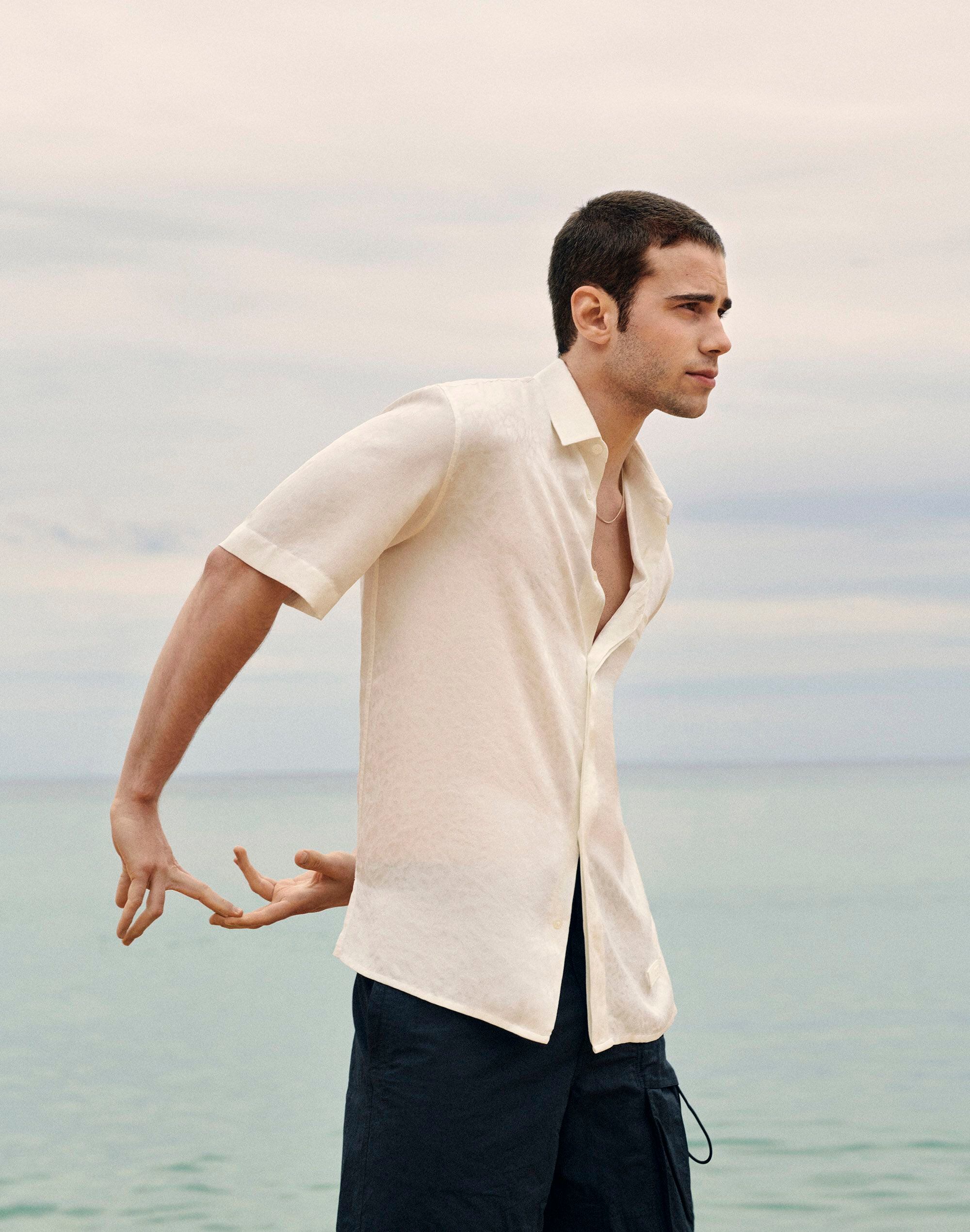 Julio Peña viste camisa blanca de seda y pantalones cortos de nailon reciclable de Dior.