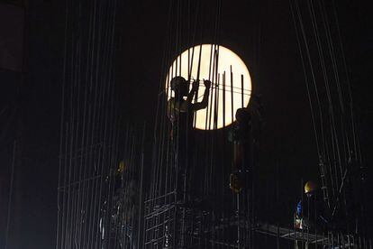 La luna llena se eleva a medida que los trabajadores de la construcción de India trabajan en una obra en Kolkata.