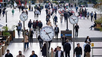 Trabajadores caminando bajo los relojes de Nash Court en el corazón del distrito financiero de Canary Wharf en Londres.