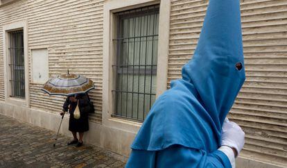 Un nazareno de la Hermandad de San Esteban pasa junto a una mujer con un paraguas camino de la Iglesia de San Esteban en Sevilla, poco antes de ser suspendida la estación de penitencia en este Martes Santo debido a la lluvia.