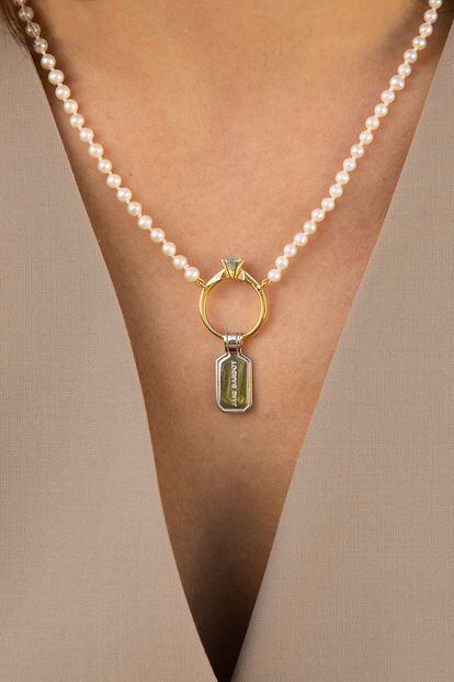 Detalle de collar de perlas con colgante y logo de la marca.