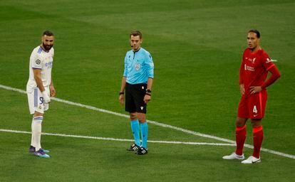 El árbitro Clement Turpin, Karim Benzema y  Virgil van Dijk esperan el veredicto del VAR ante un gol del delantero del Real Madrid en fuera de juego.  