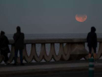 Tres personas observan el eclipse lunar parcial desde A Coruña, este viernes, en A Coruña, Galicia.