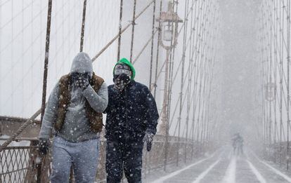 Peatones se protegen de la nieve y del viento mientras cruzan el puente de Brooklyn, en Nueva York (EE UU). 