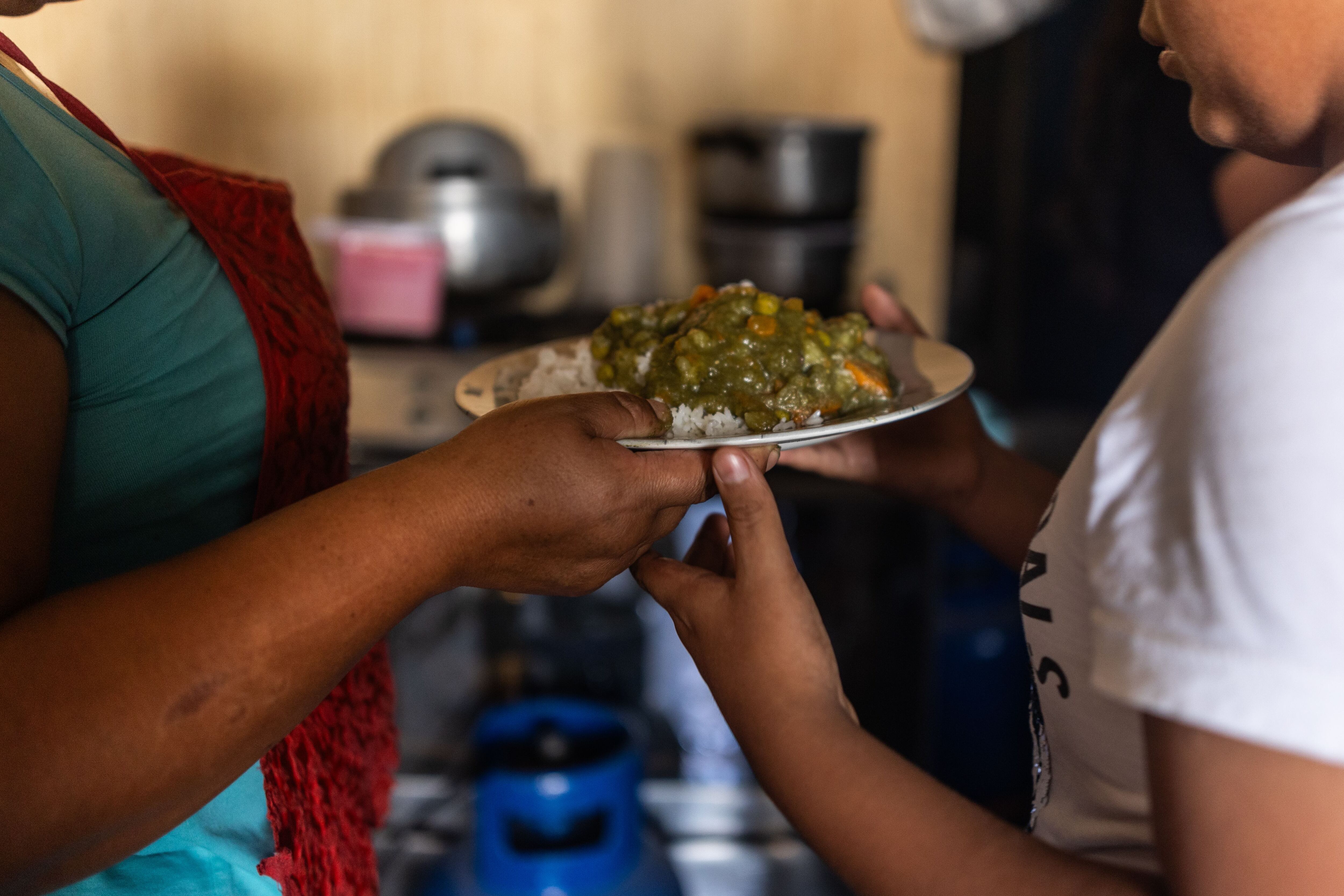Una mujer entrega un plato de comida a otra en la olla común Victor Marcial, en el asentamiento humano Nadine Heredia, en San Juan de Miraflores.