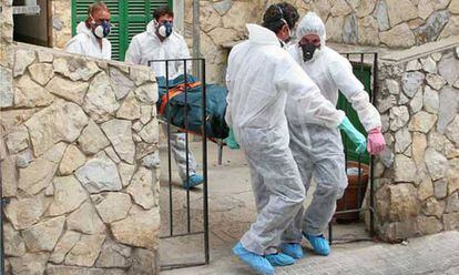 Treballadors d'una empresa funerària de Palma traslladen un cadàver equipats amb granotes i mascaretes.