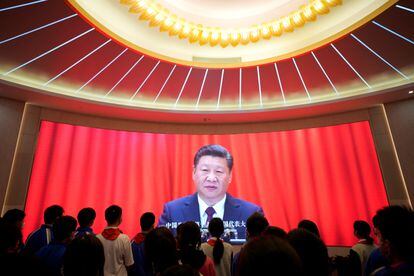 Un grupo de jóvenes frente a una pantalla en la que Xi Jinping pronuncia un discurso.