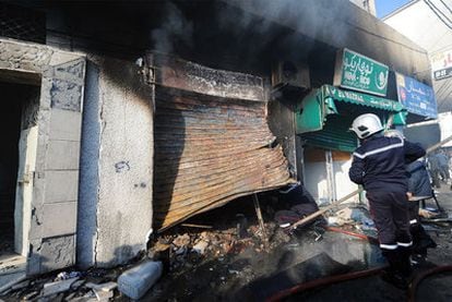 Un equipo de bomberos retira escombros de una tienda quemada durante los disturbios en Ettadhamen, en la periferia de Túnez capital.