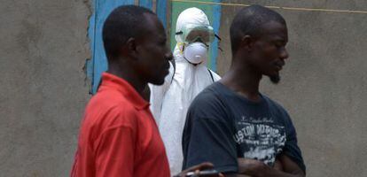 Un sanitario de la Cruz Roja de Liberia observa a dos ciudadanos en Banjol.