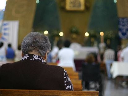 Una mujer reza sentada en un banco de una Iglesia católica.