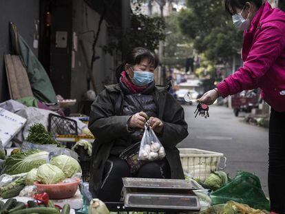 Una mujer vende sus productos protegida con una máscara en una calle de Wuhan (China).