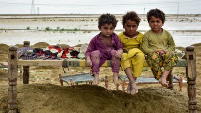 Tres niños de una familia están sentados en un charpai (cama), el 18 de agosto de este año, después de que su comunidad se mudara a un lugar más seguro cuando las inundaciones azotaron su aldea en el distrito de Naseerabad, provincia de Baluchistán, en Pakistán.