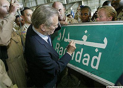 Donald Rumsfeld firma en una señal de tráfico que indica la proximidad de Bagdad en presencia de sus soldados.