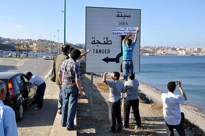 Un grupo de marroquíes escribe, el sábado, la palabra "ocupada" en la pancarta que indica la dirección de Sebta (Ceuta) que se ve al fonto.
