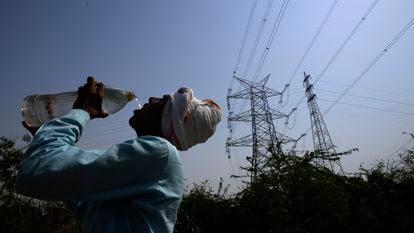 Un trabajador bebe agua junto a unos tendidos eléctricos durante la ola de calor en Nueva Delhi, India.