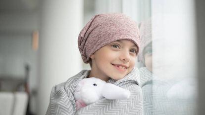 Una niña con cáncer mira por la ventana.
