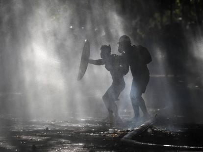Manifestantes se escudan del rocío de un cañón de agua de la policía que intenta dispersarlos en Santiago, Chile.