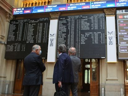 Tres hombres observan los valores económicos de la Bolsa de Madrid, en mayo.