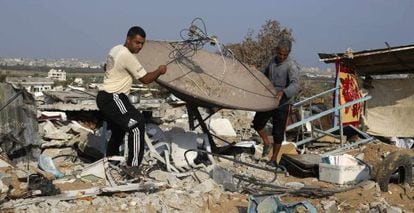 Hombres palestinos salvan una antena por satélite de las ruinas de su casa en Gaza, tras la ofensiva del verano de 2014.