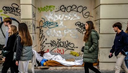 Varios jóvenes caminan frente a una persona que duerme en la calle en Madrid.